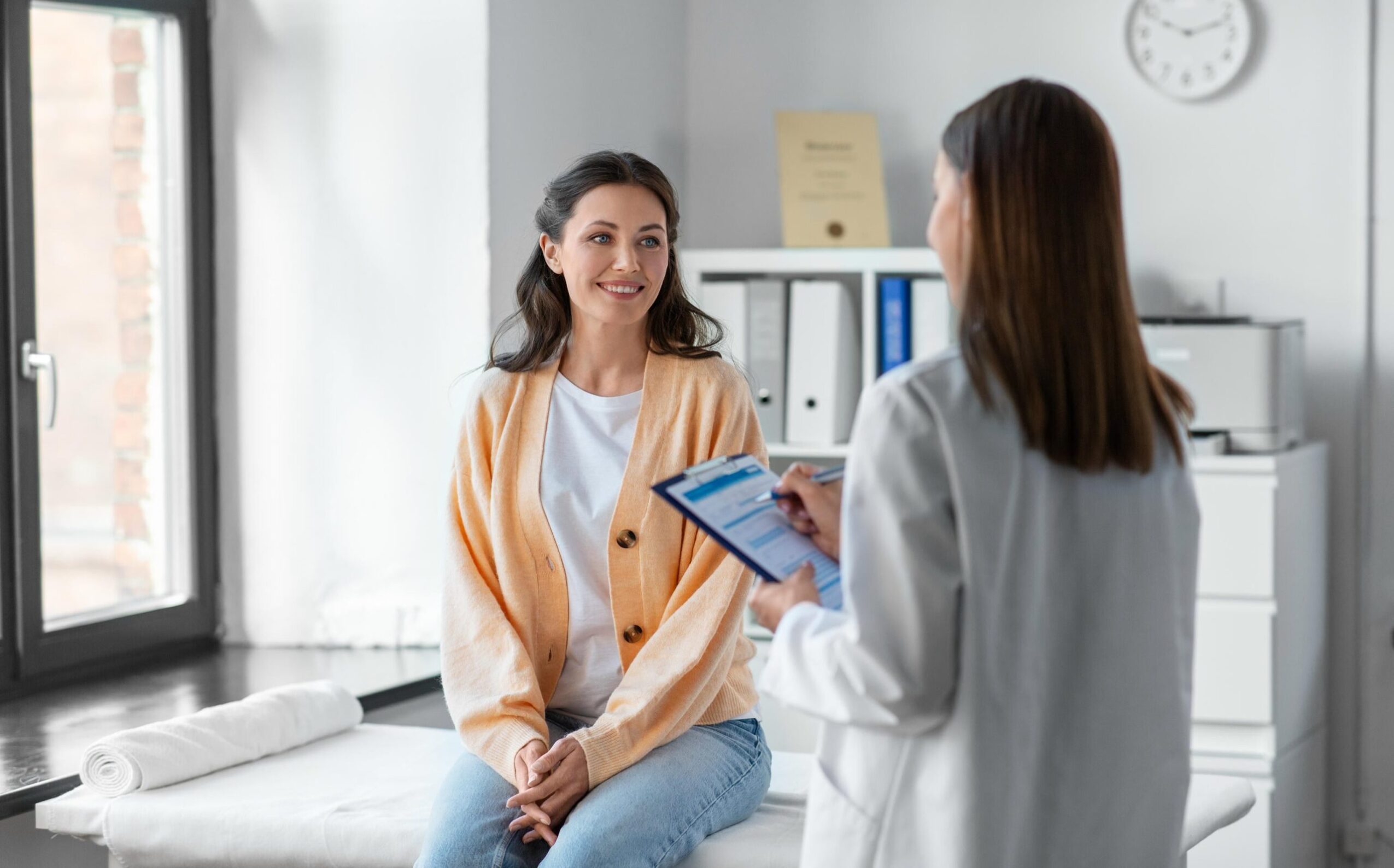 Eine Ärztin mit Klemmbrett unterhält sich im Krankenhaus mit einer lächelnden Patientin